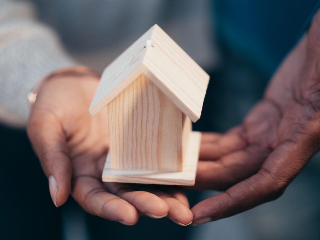 pexels-photo-7579128-7579128 Close-up of hands holding a wooden house model representing real estate or new home purchase.